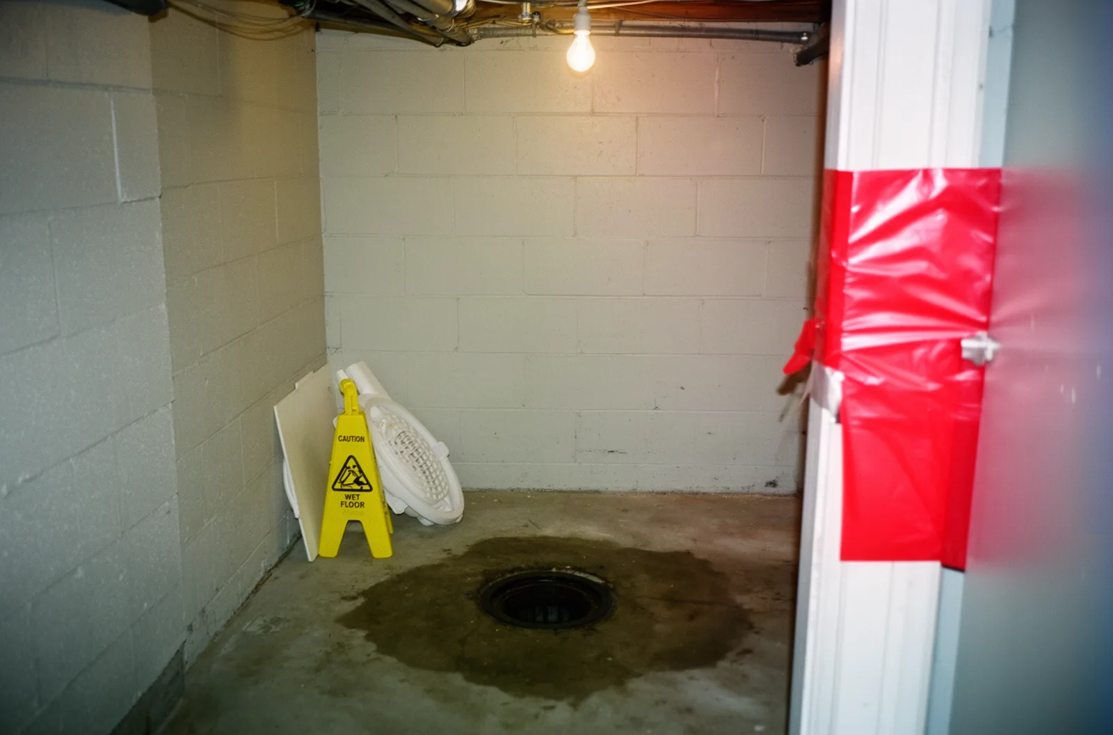 A lifted floor drain cover and containment sheeting in a basement utility room